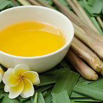 Lemongrass oil in white bowl beside long green leaves and flower