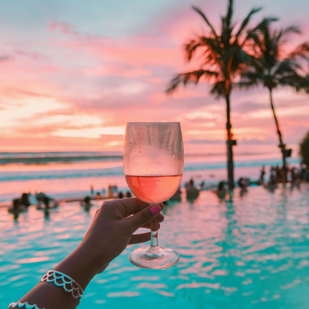 A hand holding a glass of wine in front of the pool at sunset in Bali, Indonesia.