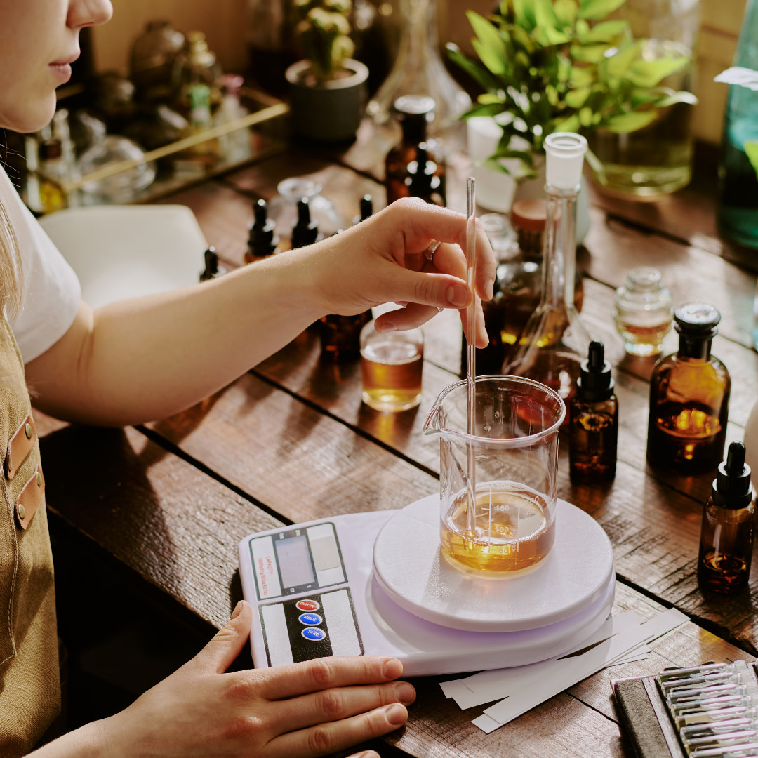 A person in an apron is using a scale to measure the amount of liquid in a glass