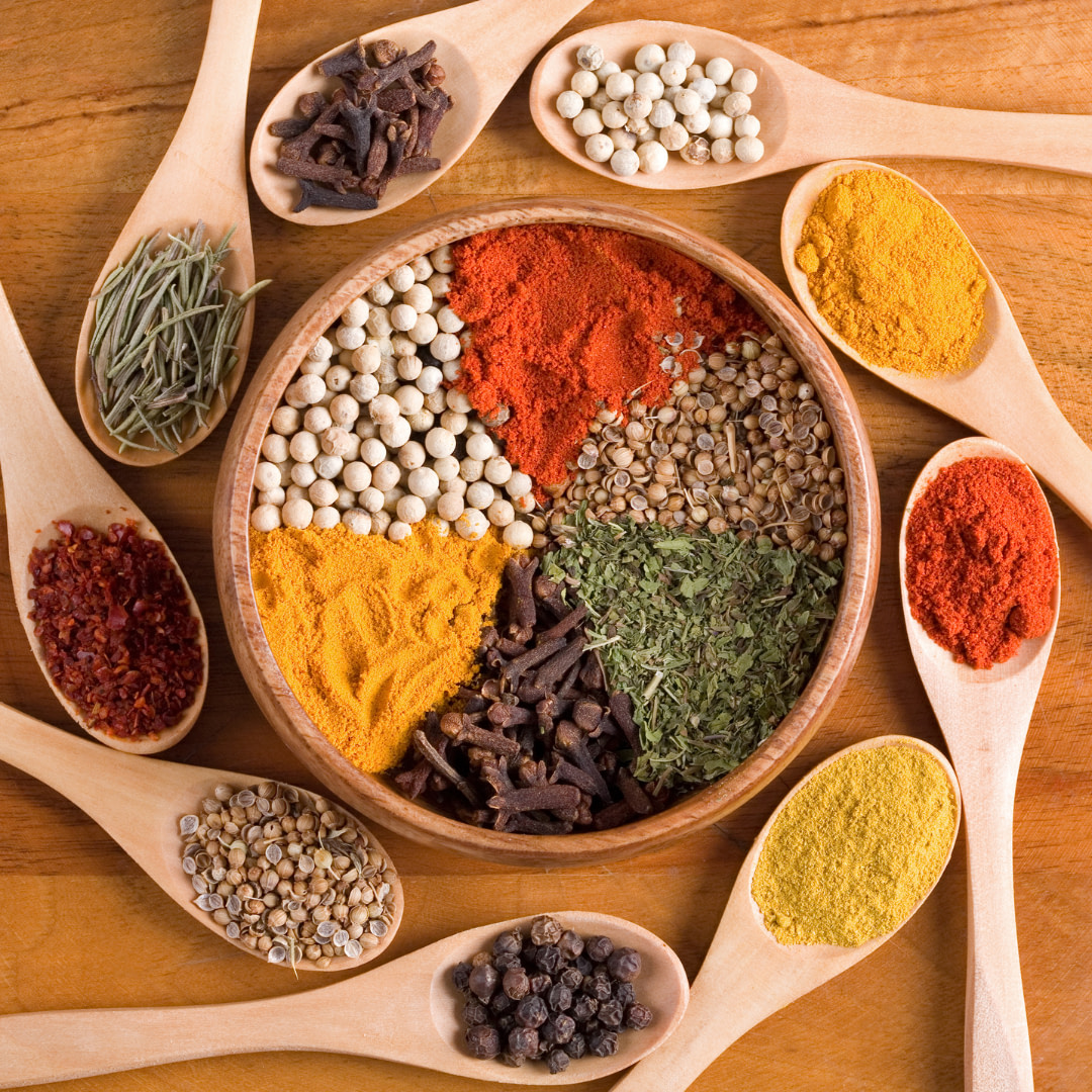 various spices and herbs in wooden spoons on a wooden table