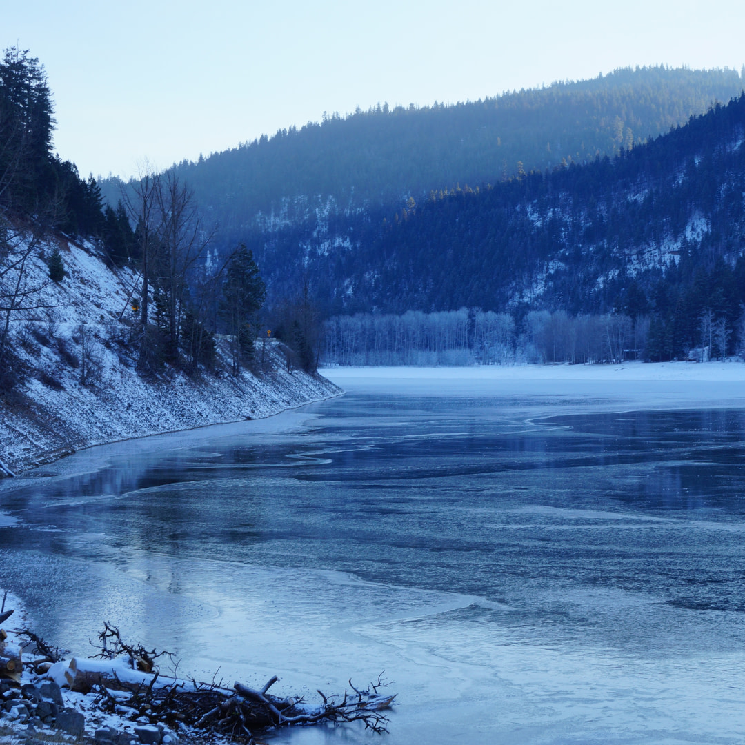 a frozen lake in the mountains with snow on the ground