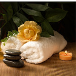 towels, candles and a bottle of oil sit on a bamboo mat