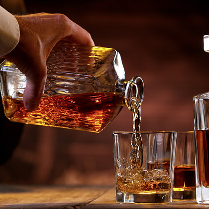 a person pours whiskey into a glass on a wooden table