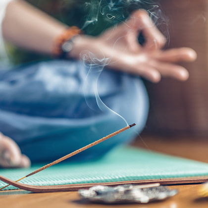 A person meditating with incense sticks on the floor