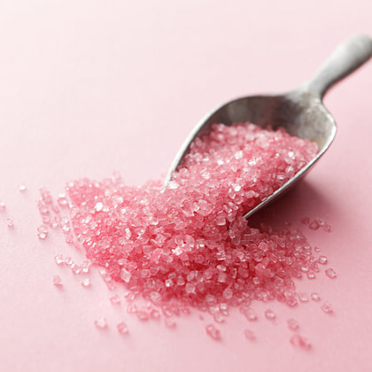 a spoon full of pink sugar on a pink background