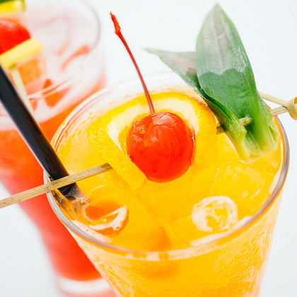 a red drink with a pineapple garnish and colorful umbrellas