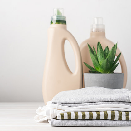 Two bottles of laundry detergent sit behind a succulent in a gray pot and a neatly folded stack of clothing.