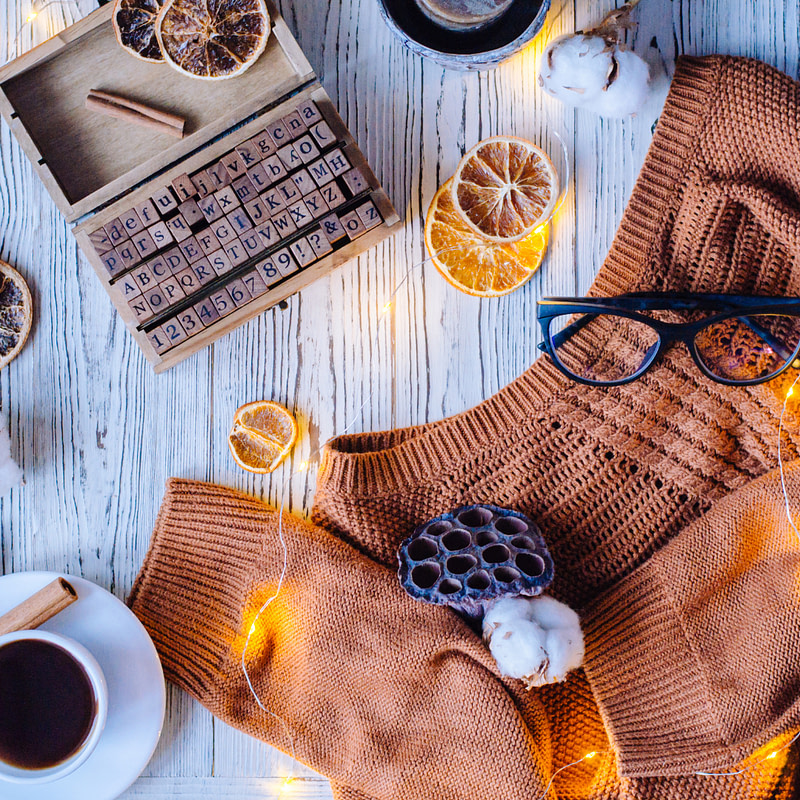 top view of a cozy sweater, coffee cup and cotton wool on a white wooden table with Christmas lights