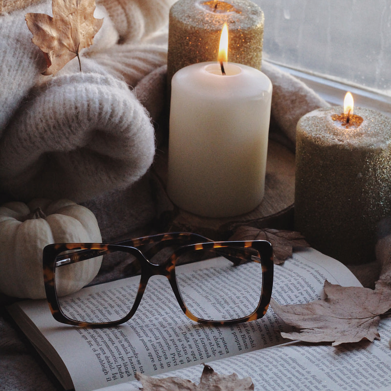 candles, an open book, and autumn leaves on a window sill