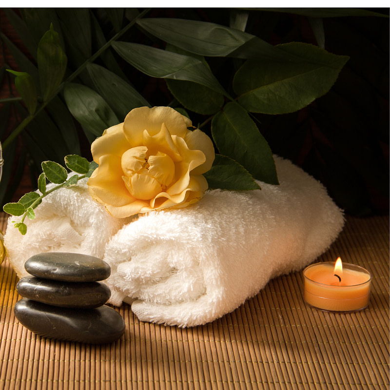 towels, candles and a bottle of oil sit on a bamboo mat