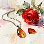 a chain jewelry with an amber colored pendant and heart shape next to a red rose