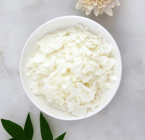 Soy wax flakes in a bowl next to a flower and leaves