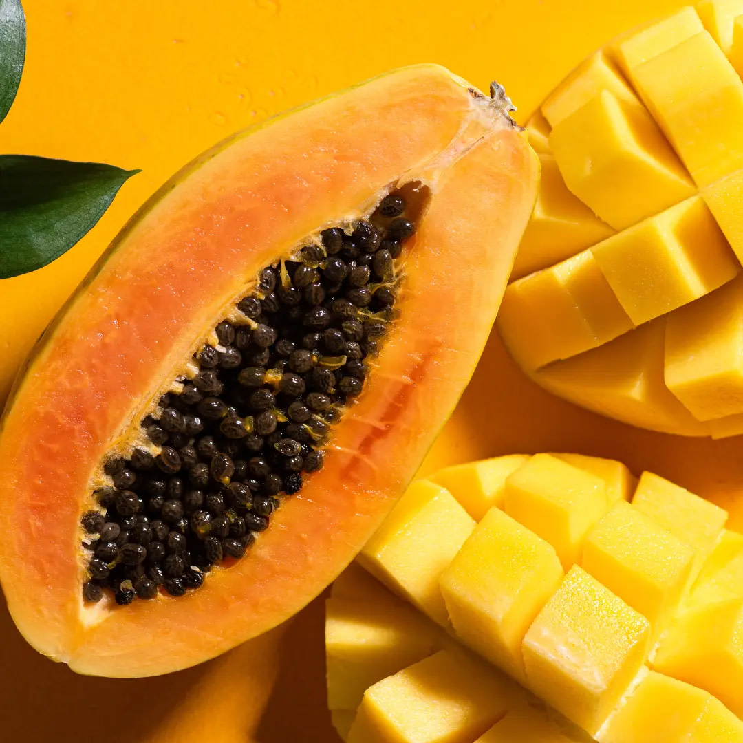 Fresh papaya and mango fruits positioned on a sunny yellow backdrop.