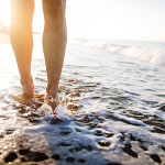 the feet of a person walking on the beach at sunset