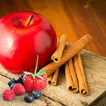 apples, cinnamon and berries on wood surface