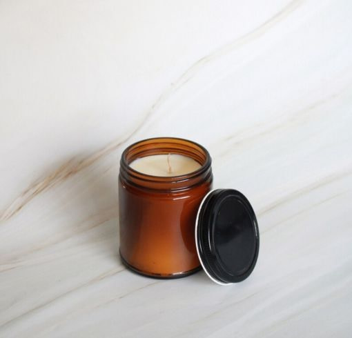 an orange candle with a black lid sitting on a marble surface